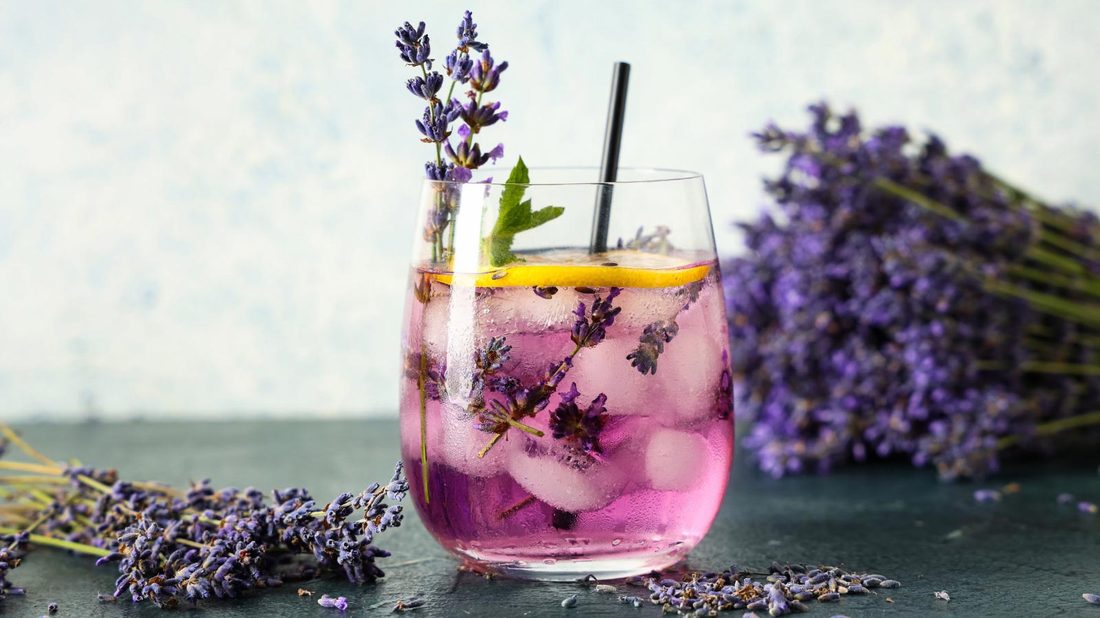 Glass of fresh lavender lemonade with mint and flowers on dark table.