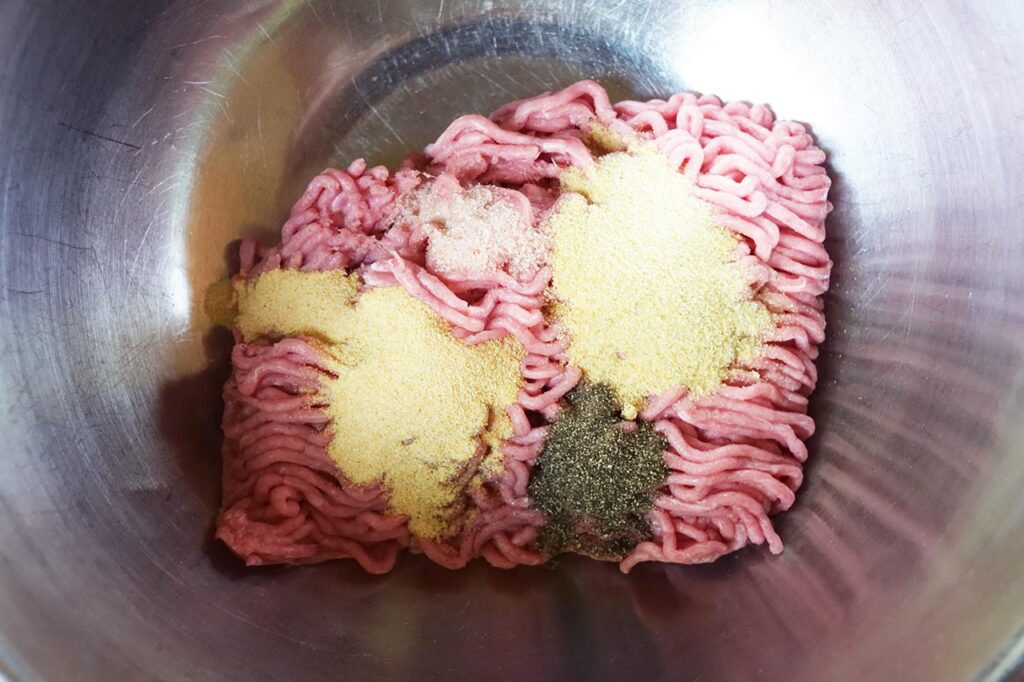 A mixing bowl with ground turkey and spices in it.