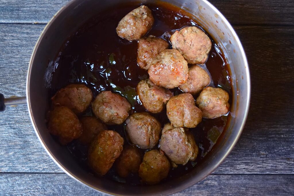 Meatballs added to a pot of glaze.