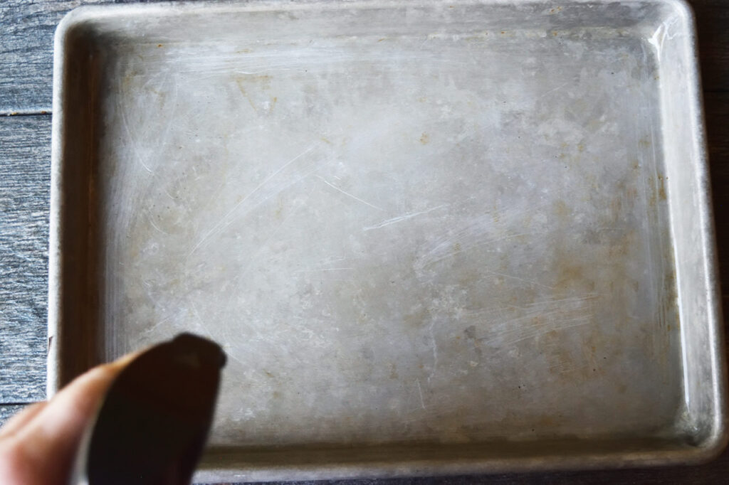 Spraying oil on a sheet pan with an oil sprayer.