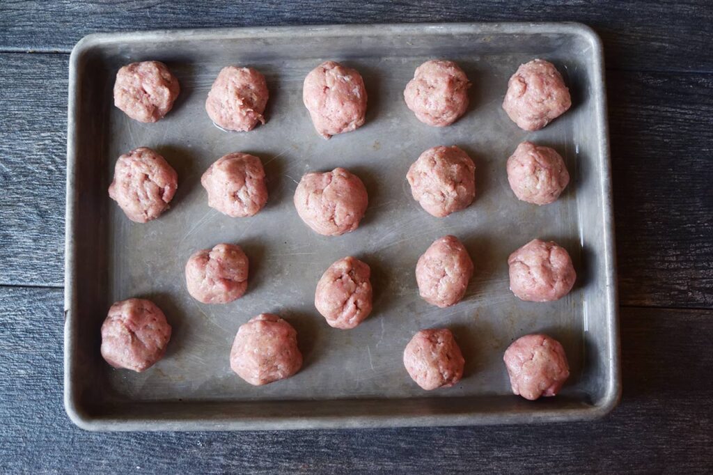 Raw, rolled meatballs on a baking sheet.