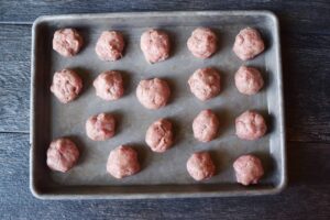 Raw, rolled meatballs on a baking sheet.