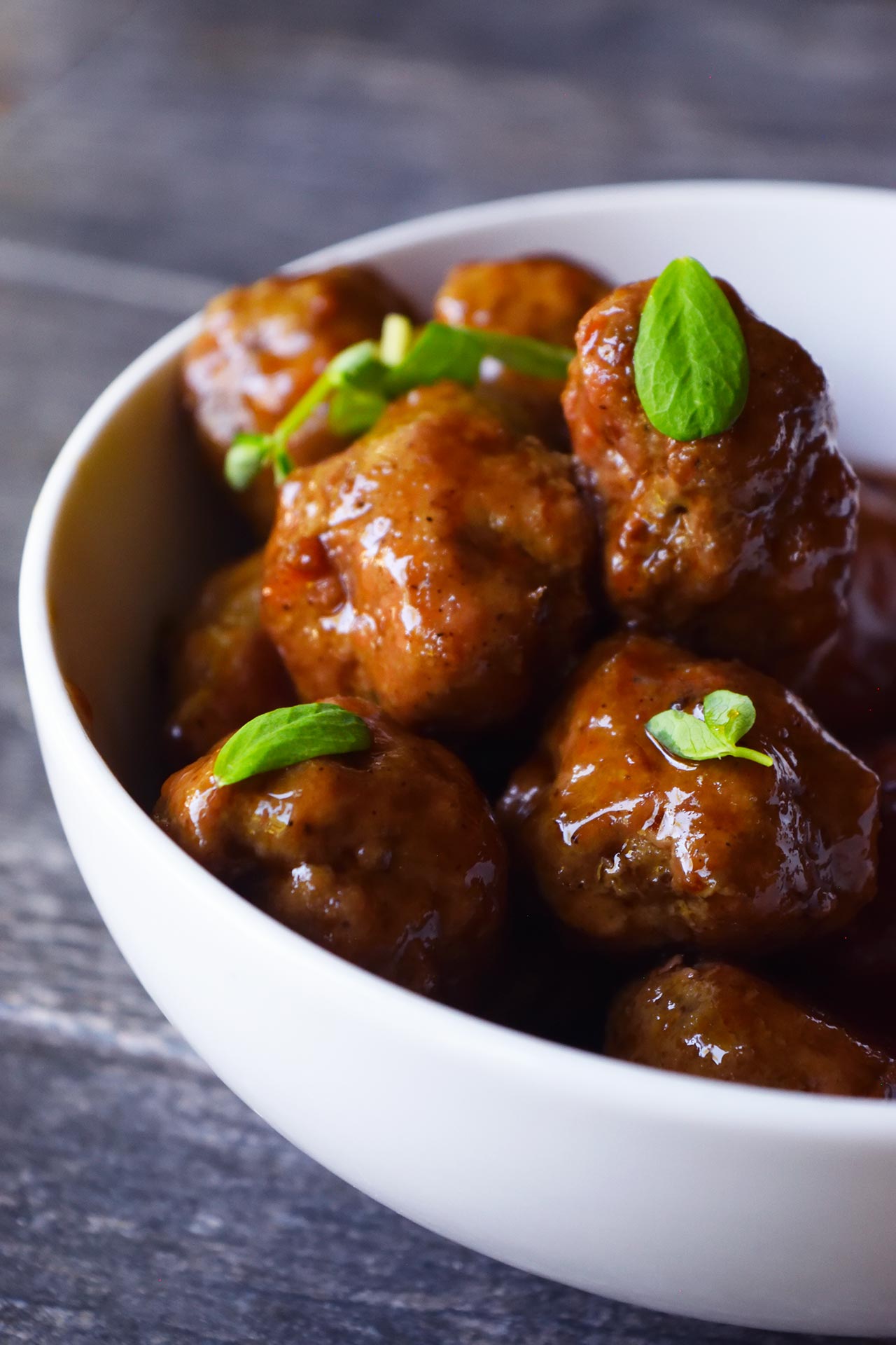 A side view of a bowl of glazed, Sweet And Sour Meatballs.