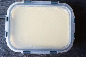 A lid covering the plastic wrap and custard on a freezer-safe dish.