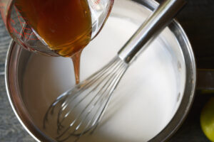 Pouring sweetener into coconut milk in a pot with a whisk.