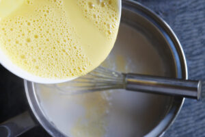 Returning the tempered eggs to the remaining milk in the pot.