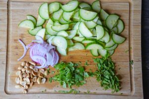 Thai cucumber salad vegetables, nuts and herbs on a wood cutting board.
