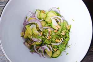 Thai cucumber salad vegetables, peanuts, and fresh, chopped herbs in a large, white mixing bowl.