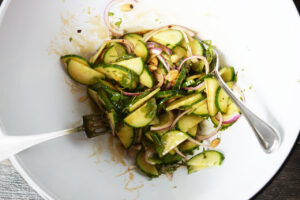 Thai cucumber salad tossed with dressing in a large, white mixing bowl.