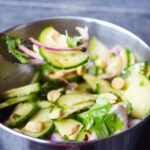 A fork lifts a bit of Thai cucumber salad. from a bowl.