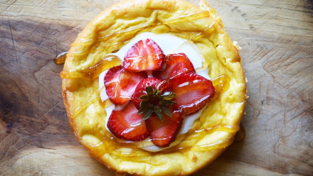 Overhead view of a strawberry topped yogurt cake on a wood surface.
