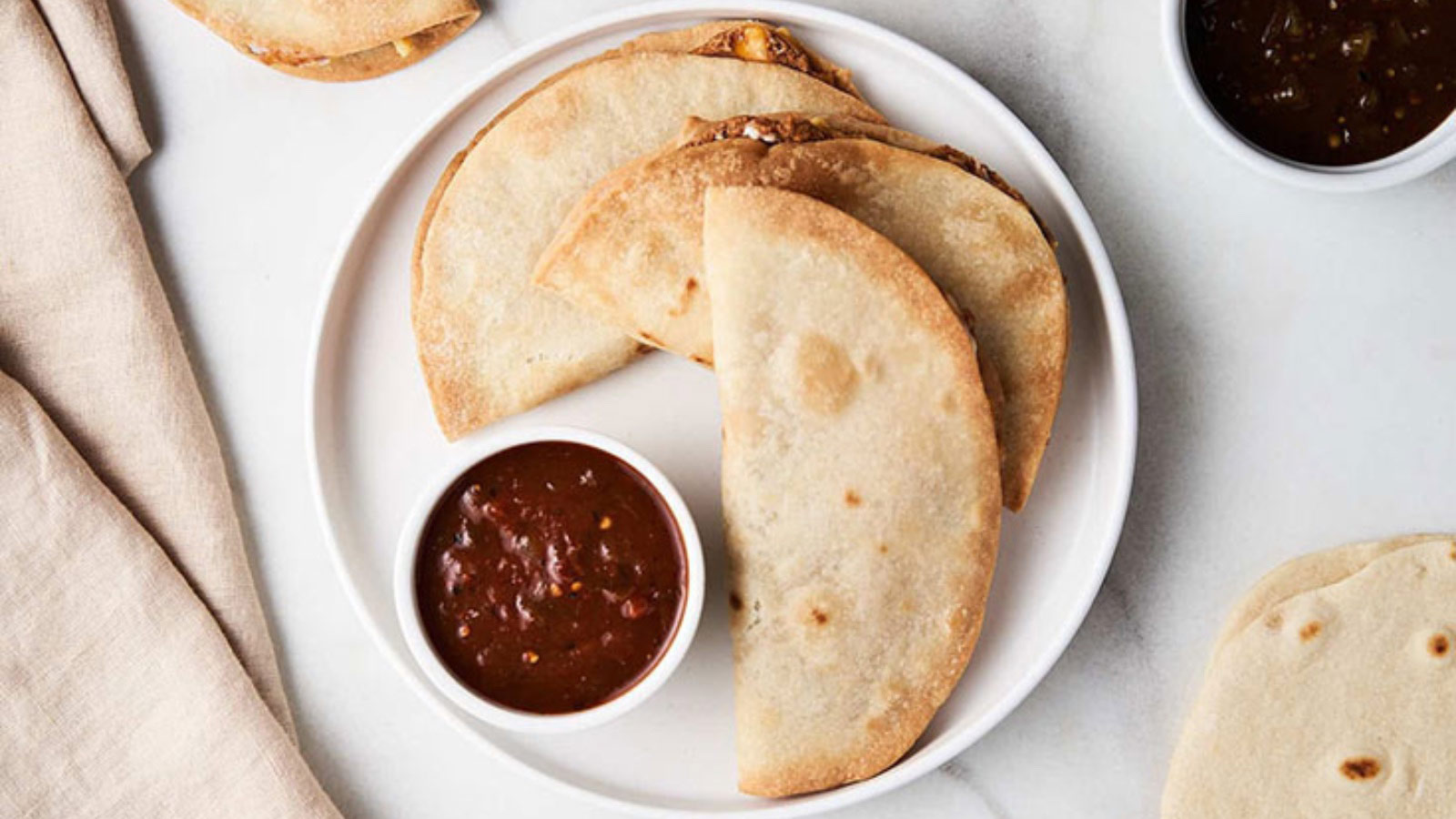 A white plate holds three air fryer quesadillas with a small bowl of sauce.