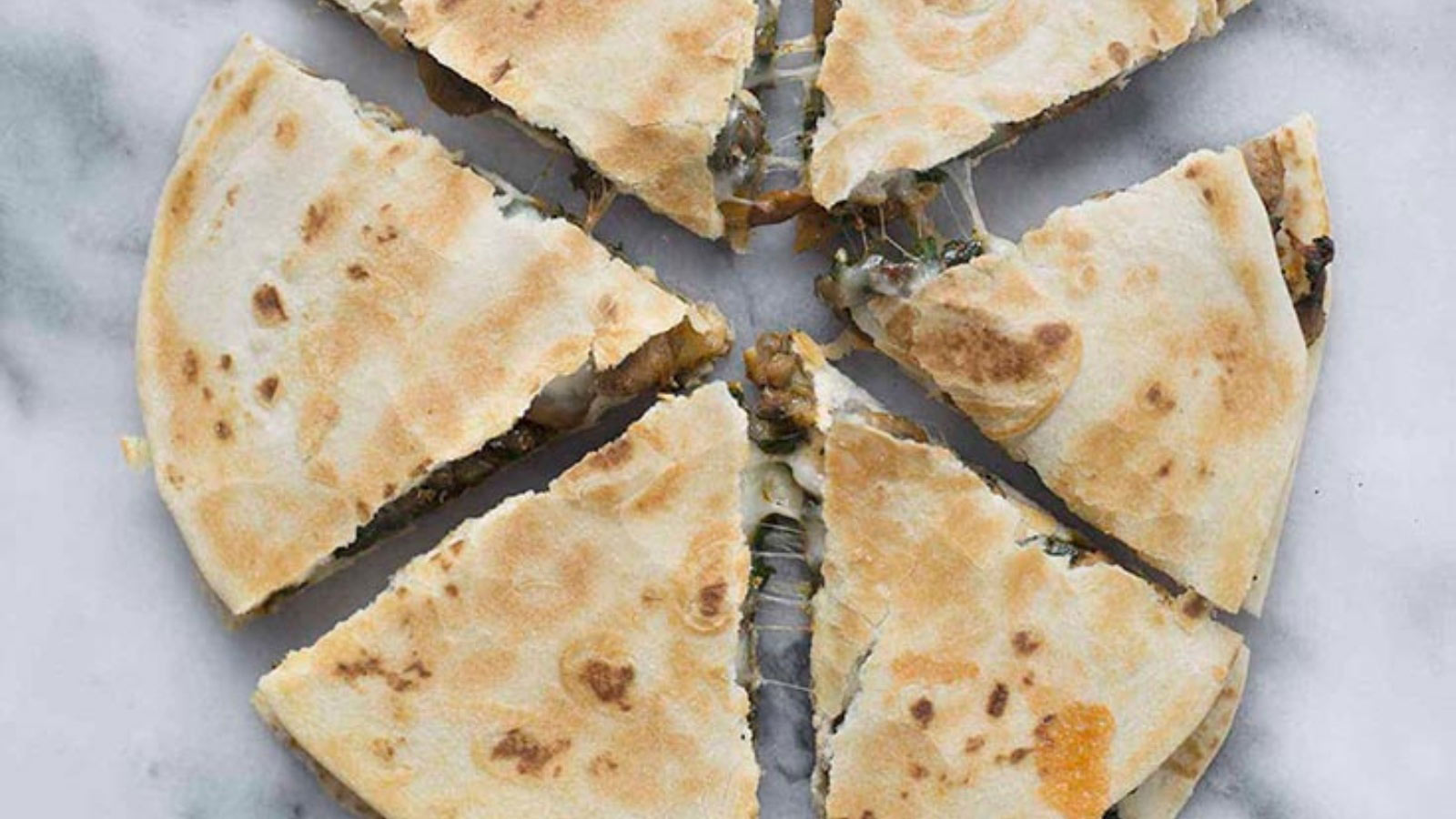 A sliced lentil mushroom and spinach quesadilla on a white marble surface.