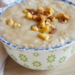Side view of a decorative bowl filled with banana pudding, garnished with walnut pieces.