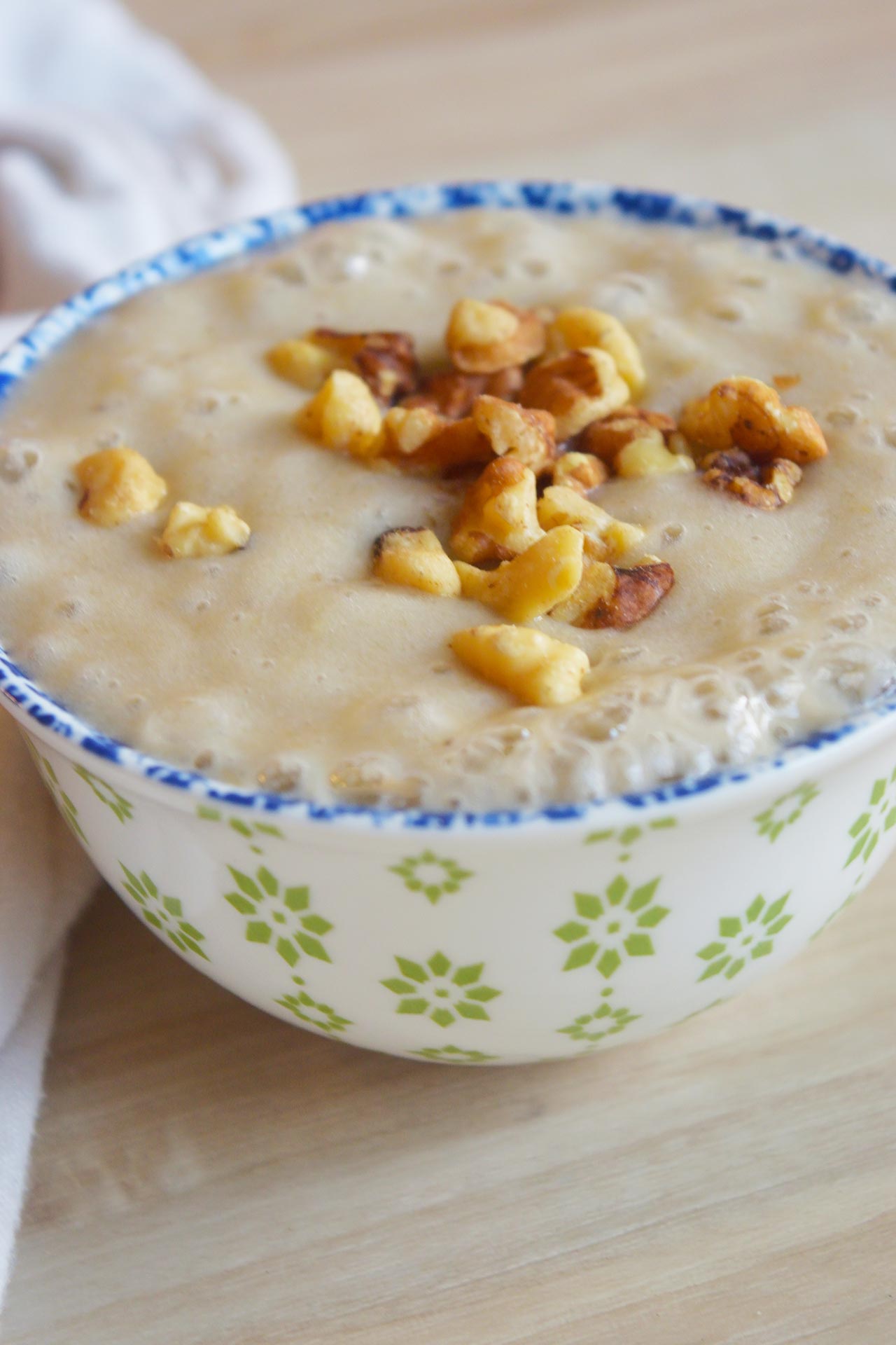 Side view of a decorative bowl filled with banana pudding, garnished with walnut pieces.