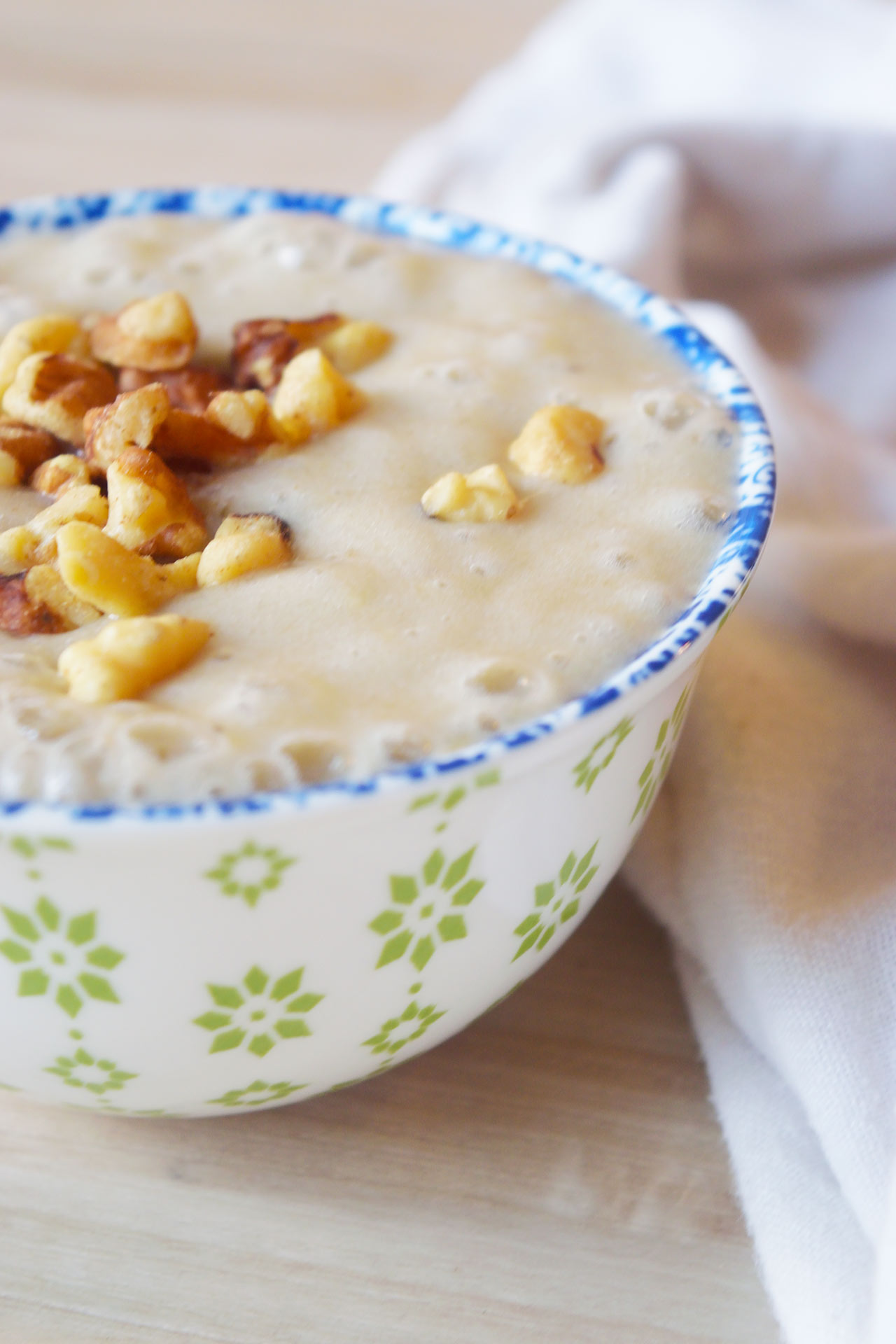 Partial side view of a small, decorative bowl filled with banana pudding topped with walnut pieces.