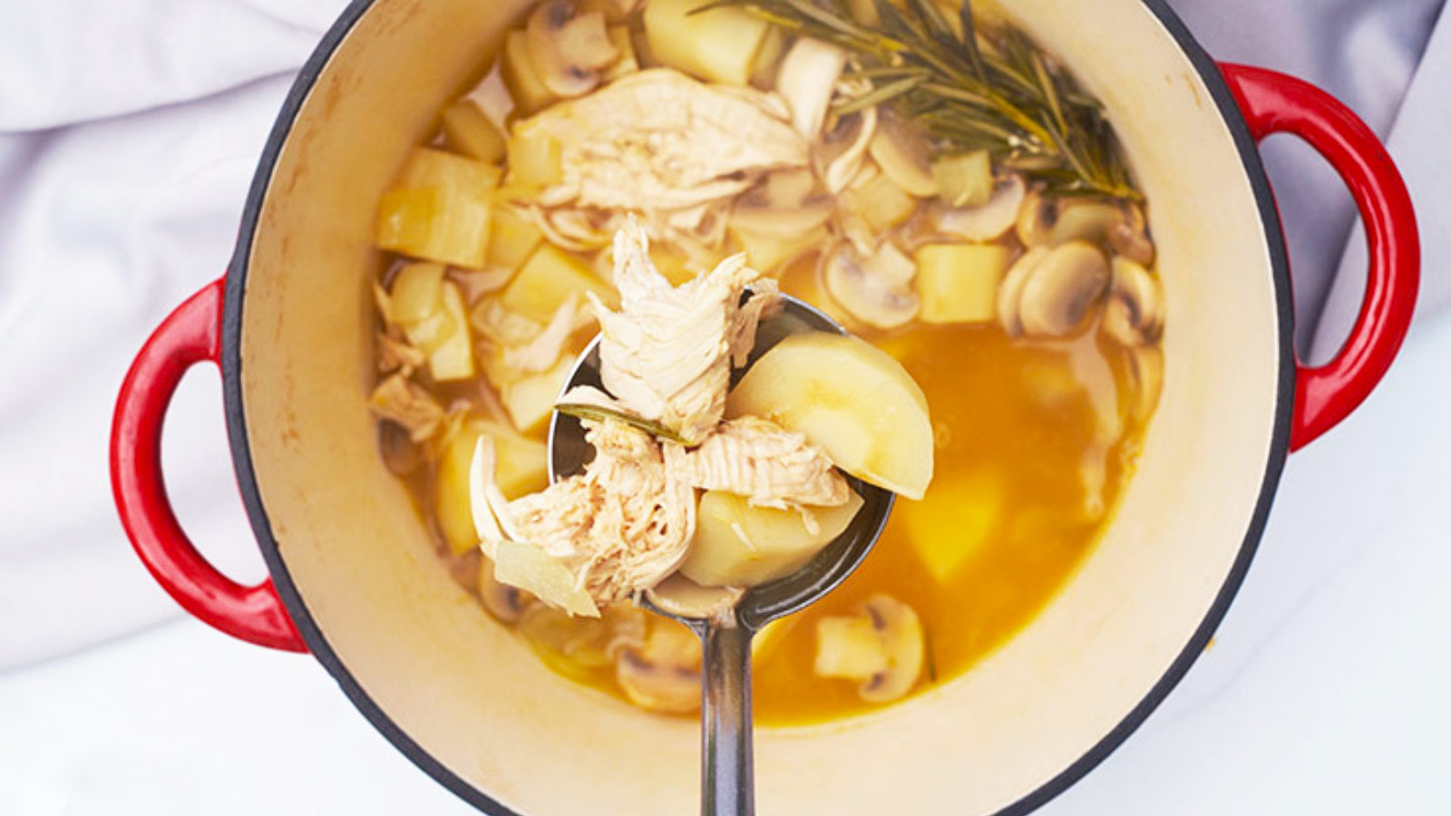 A ladle lifting some Chicken And Parsnip Soup out of a stockpot.