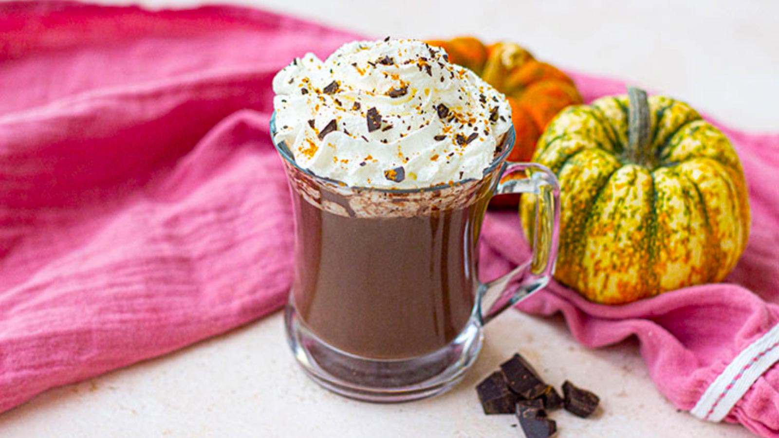 Whipped cream added to the top of a glass mug filled with pumpkin hot chocolate.