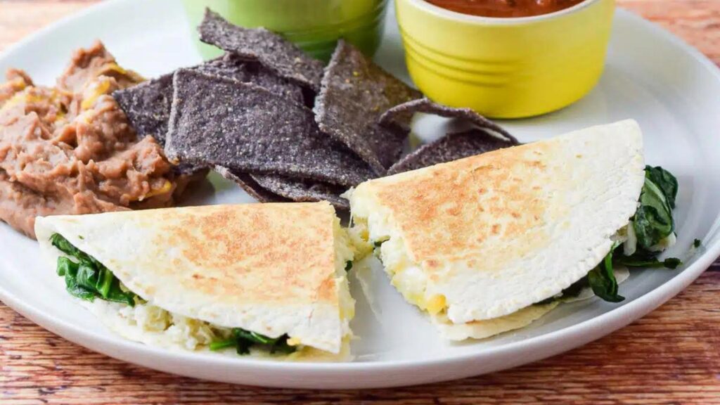 A crab quesadilla on a plate with blue corn chips and refried beans.