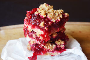 Stacked cranberry bars sitting on parchment and a wood surface.