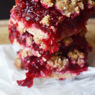 Closeup of a stack of three cranberry bars on white parchment paper.