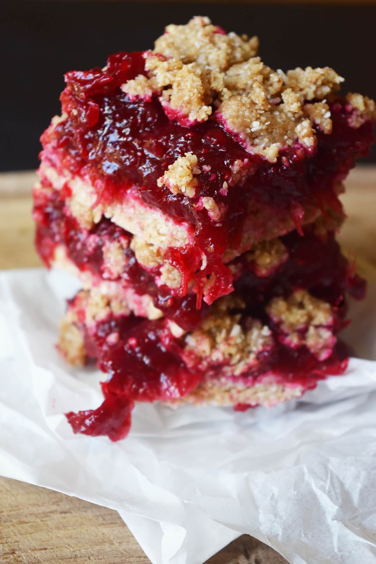 Closeup of a stack of three cranberry bars on white parchment paper.