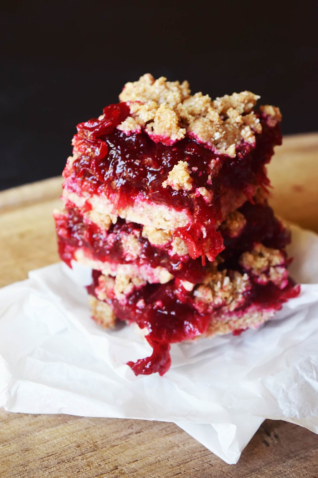 Front view of a stack of cranberry bars on a wood surface with parchment.