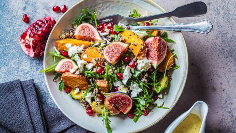 Warm autumn quinoa salad with baked vegetables (sweet potato, Brussels sprouts), figs, feta cheese and pomegranate, top view.