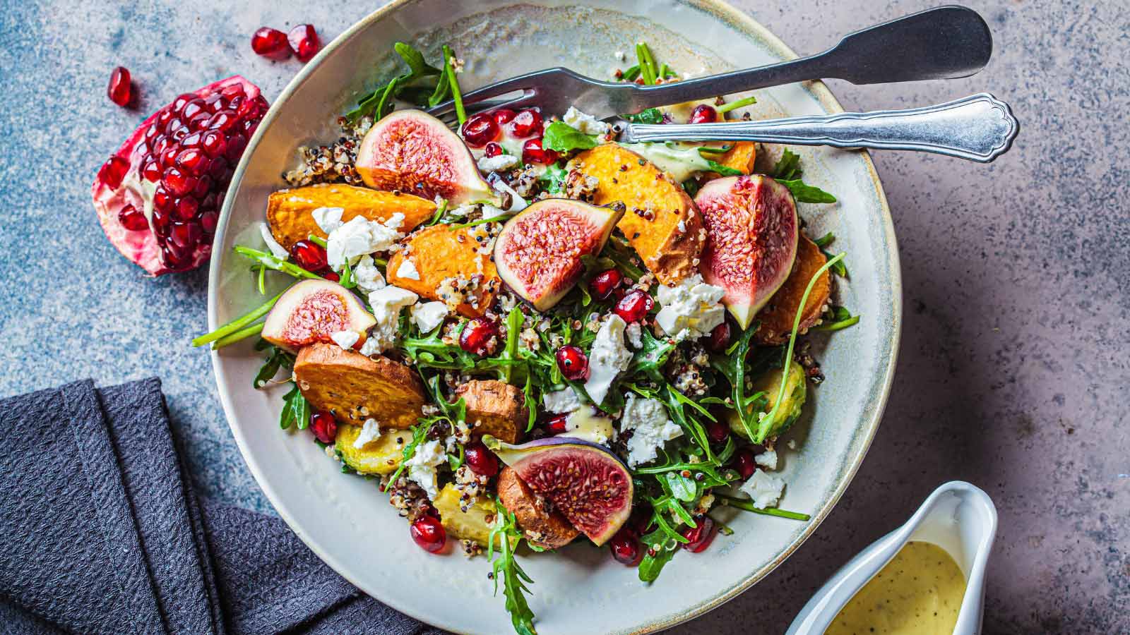 Warm autumn quinoa salad with baked vegetables (sweet potato, Brussels sprouts), figs, feta cheese and pomegranate, top view.