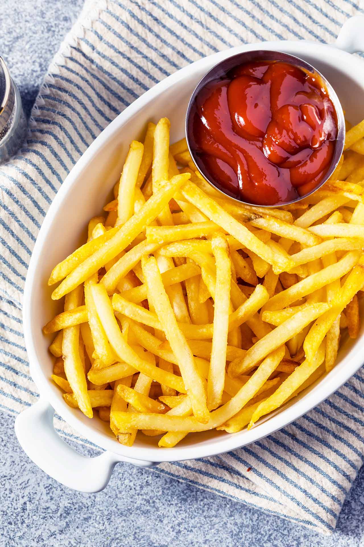 Homemade Golden French Fries with Tomato Ketchup and salt in a white, oval dish.