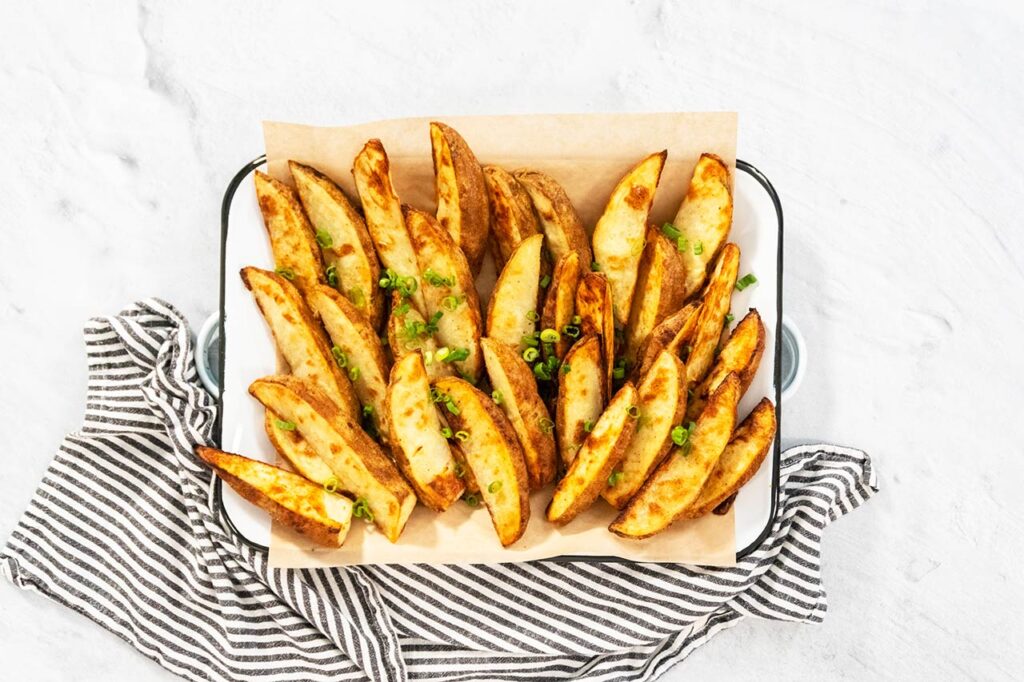 Flat lay. Freshly baked potato wedges with spices on a white serving tray.