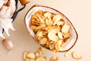 Overhead view of a bowl full of garlic chips with a few spilled over onto a beige surface.