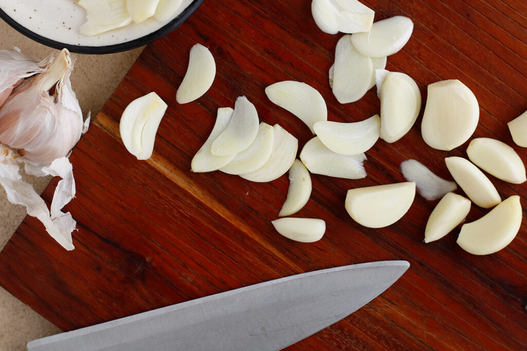 Sliced garlic on a cutting board with a knife.