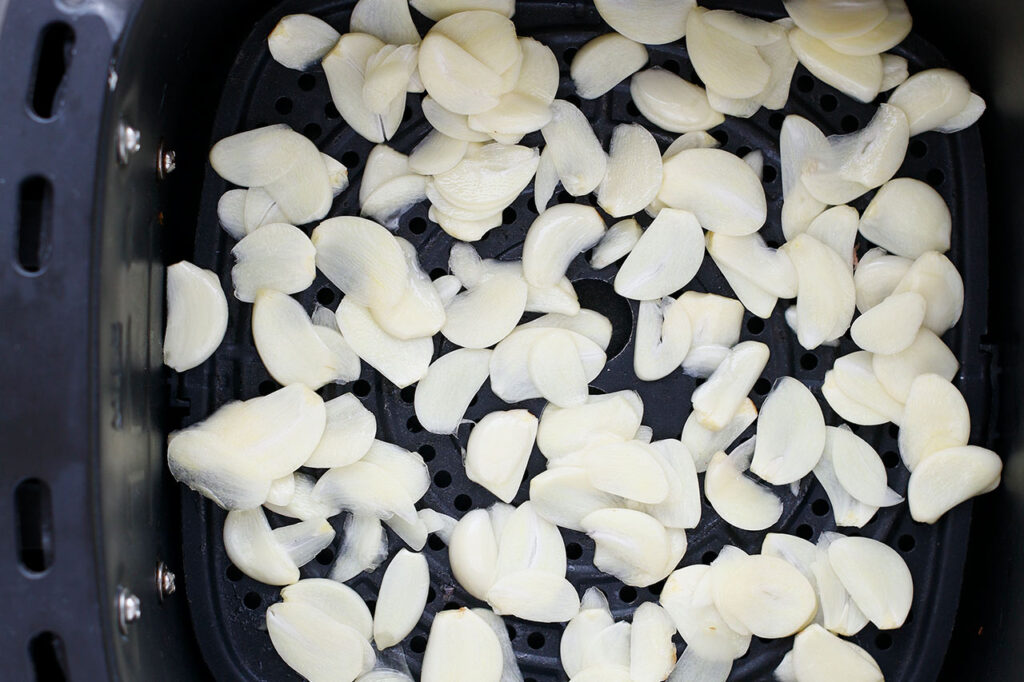 Sliced garlic laid out in a single layer in an air fryer basket.