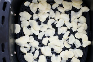 Sliced garlic laid out in a single layer in an air fryer basket.