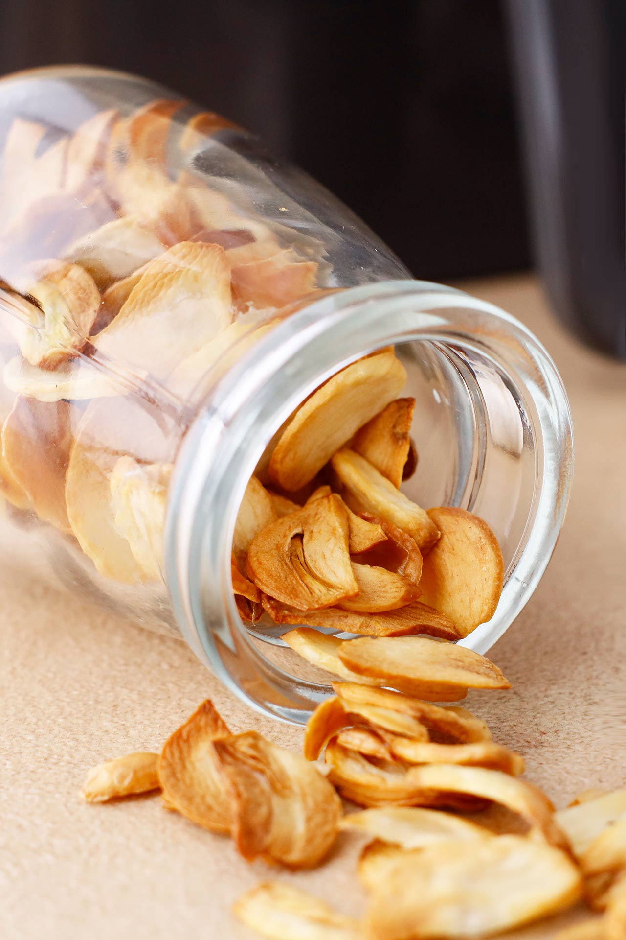 Side view of a jar full of garlic chips tipped over with garlic chips spilling out.