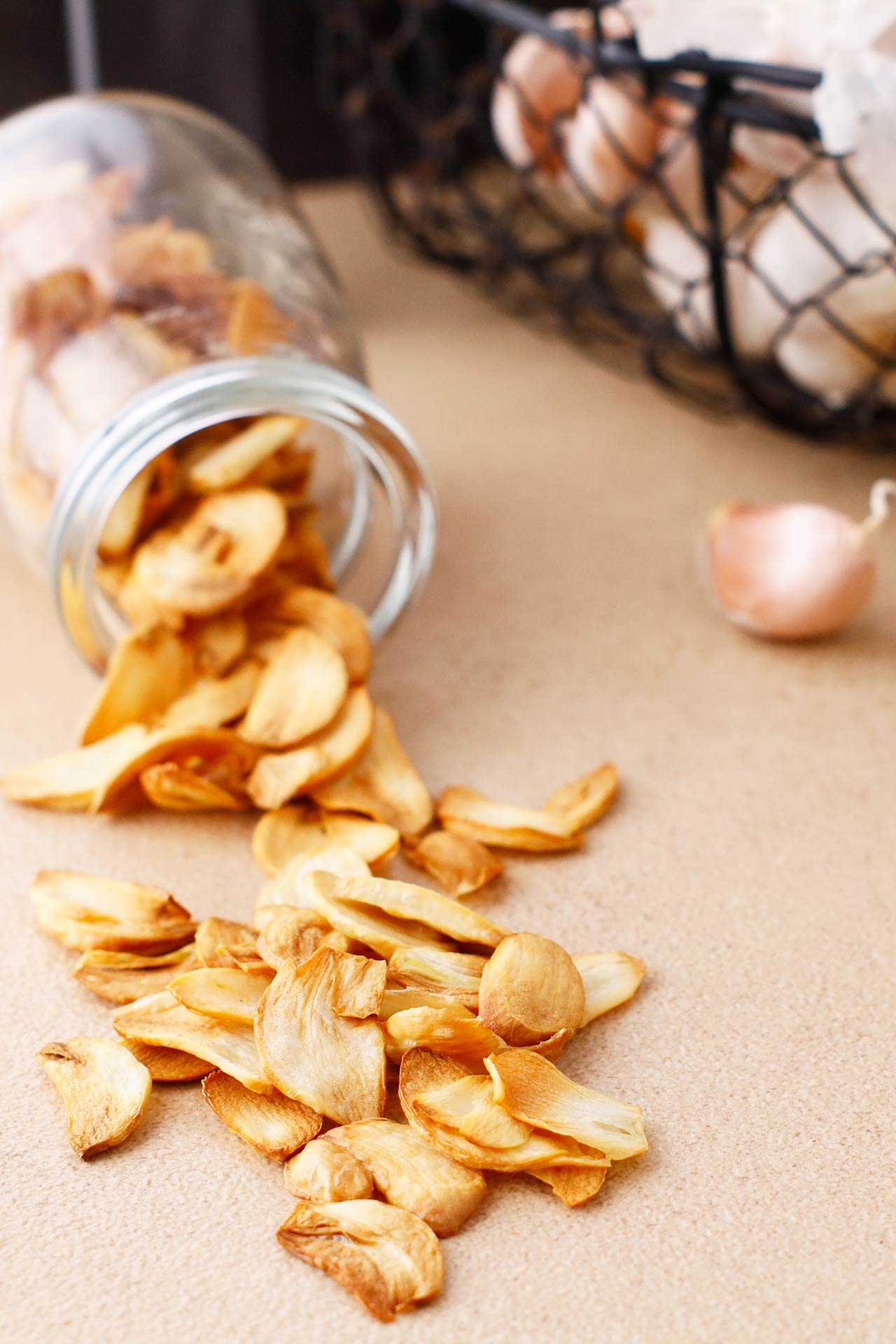 Front view of a jar full of garlic chips tipped over with garlic chips spilling out.