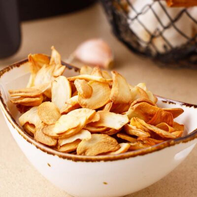 Side view of a ceramic bowl full of garlic chips.