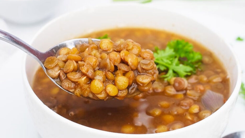 A spoon lifts some german lentil soup out of a white bowl.