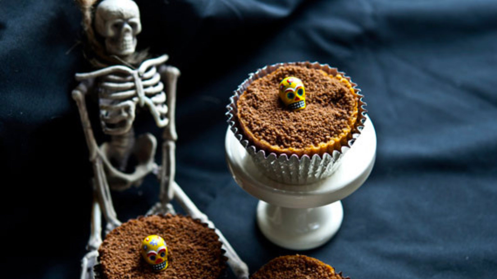 Graveyard dirt cupcakes. One on a cupcake pedestal. A small skeleton sits next to it.
