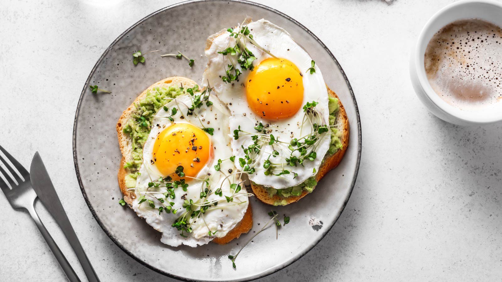 Avocado Egg Sandwiches and coffee for healthy breakfast. Whole grain toasts with mashed avocado, fried eggs and organic microgreens on white table.