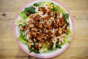 Beans and chicken layered over lettuce in a salad bowl.