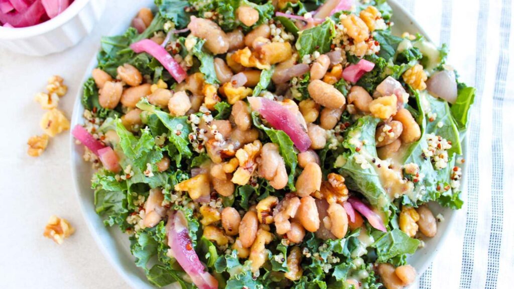 Overhead view of a white bowl filled with Kale Salad With Walnuts And Butter Beans.