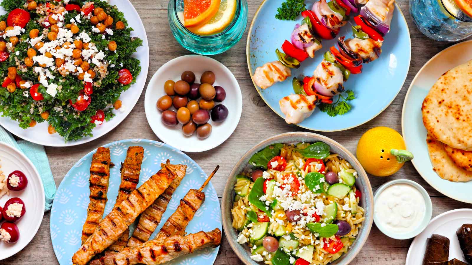 Summer Mediterranean theme food table scene. Top view on a wood banner background. Grilled skewers, salads, snacks, pita and tzatziki.