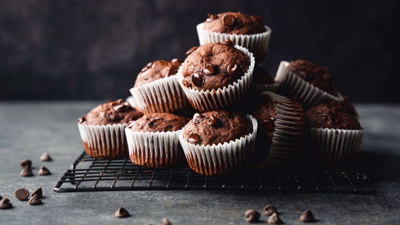 Close up of many chocolate muffins on a dark gray background.