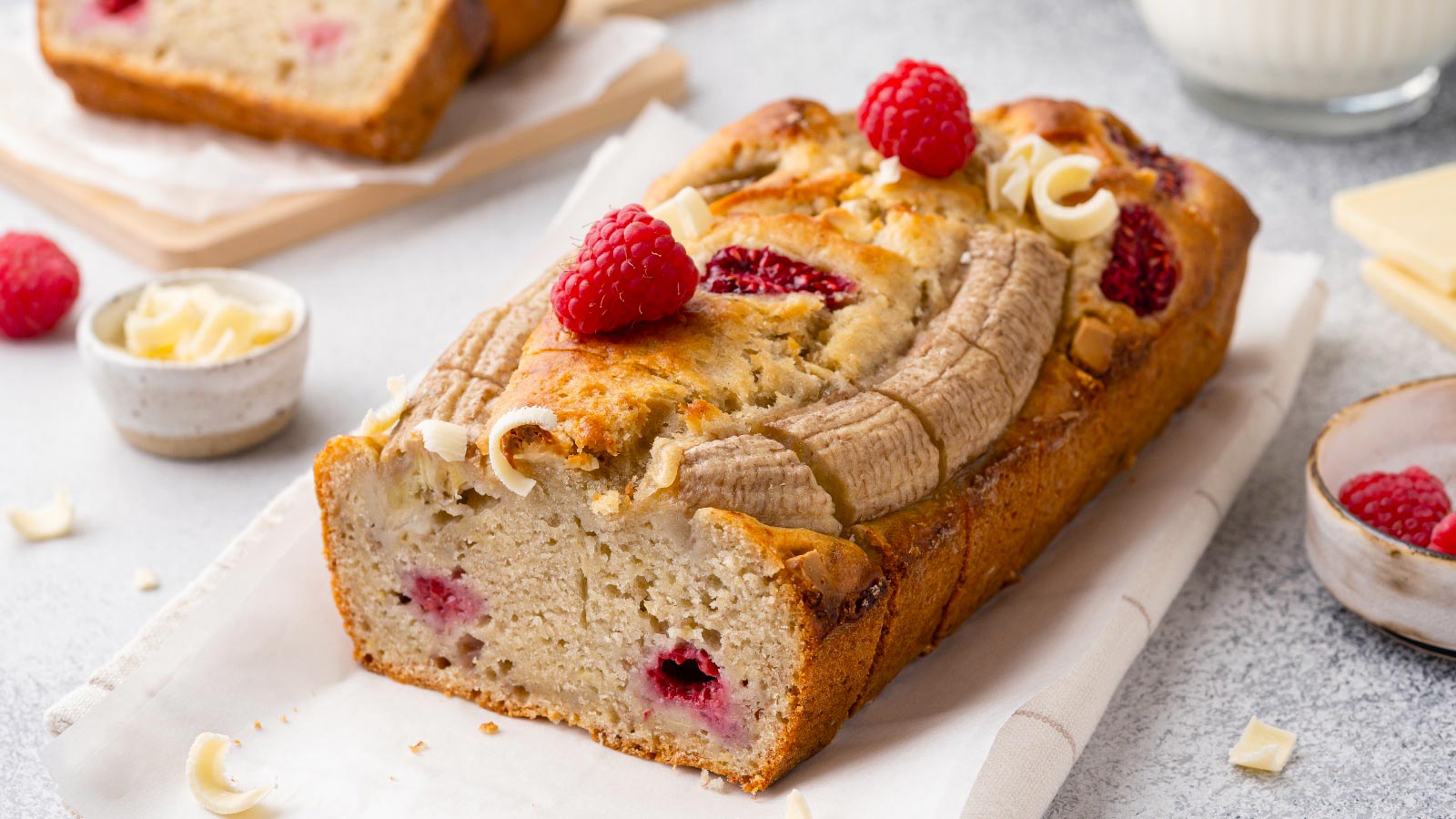 Banana bread with fresh raspberry and white chocolate. Fruit loaf cake sliced in pieces and served on kitchen napkin. Grey concrete table. Close up view.