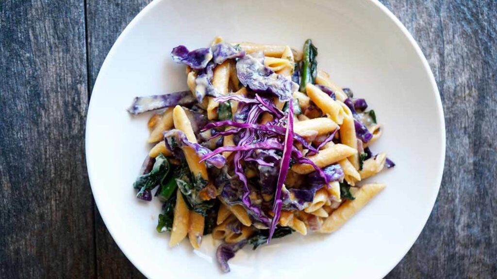 An overhead view of a white bowl partially filled with red cabbage peanut pasta.