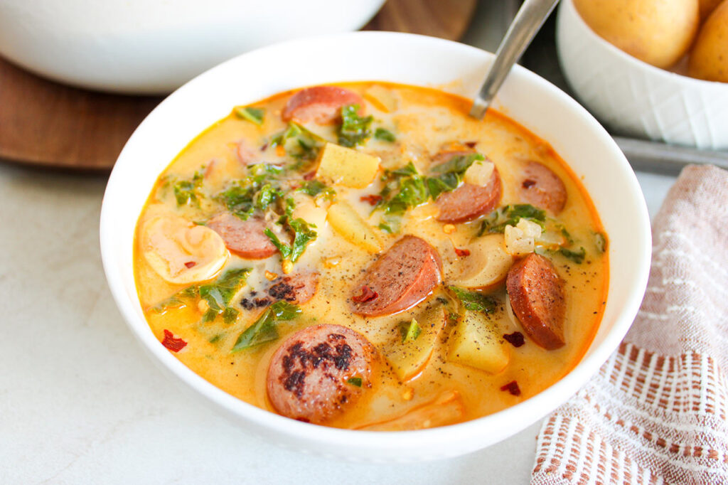 A white bowl with a spoon, filled with Sausage, Kale And Potato Soup.
