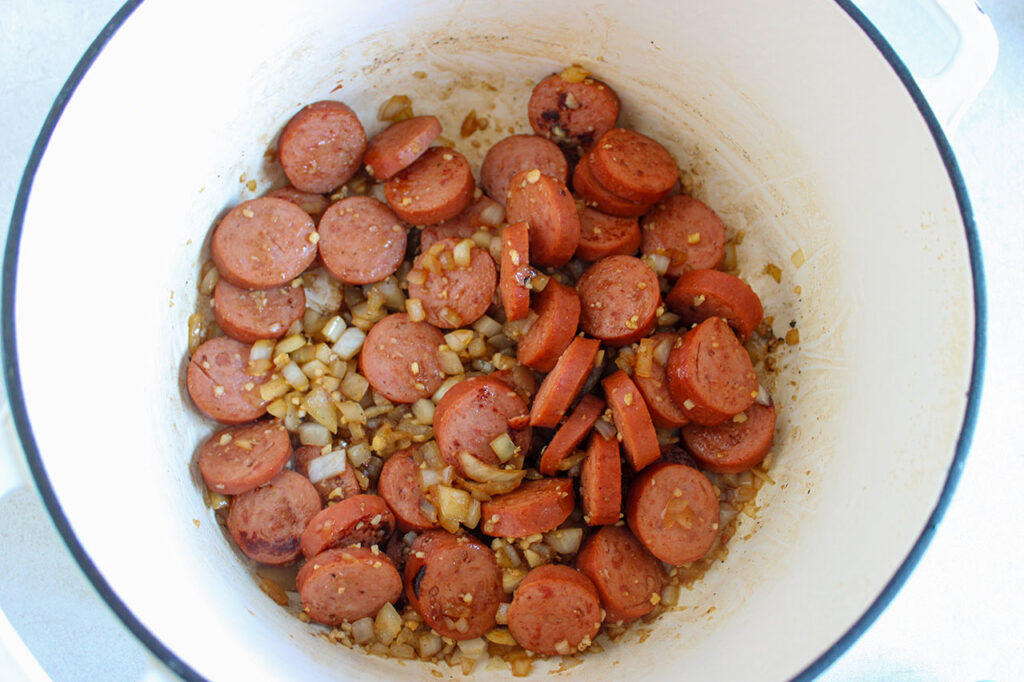 Sliced sausage and sautéd onions in a mixing bowl.