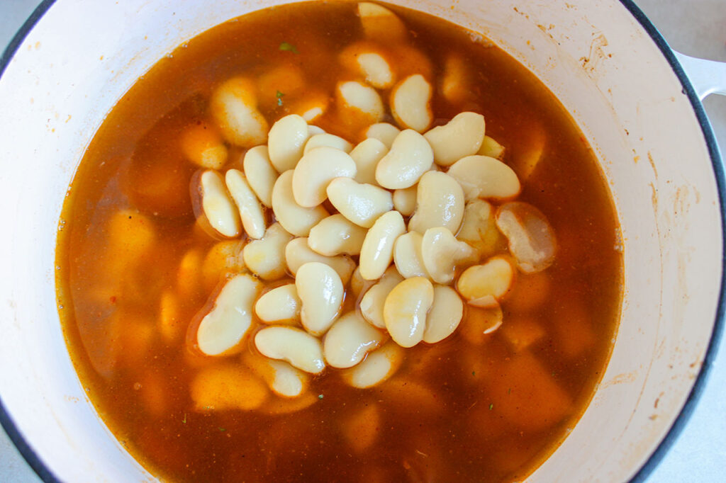 White beans and broth added to a bowl with sausage and onions in it.